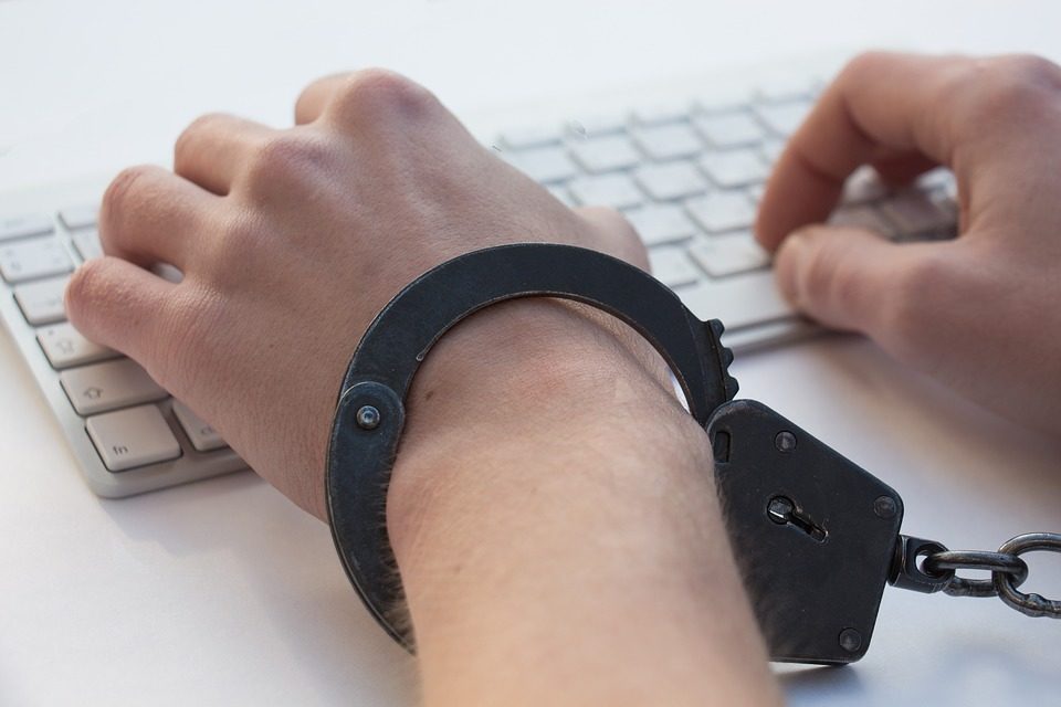 L'image représente des mains enchaînées par des menottes sur un clavier d'ordinateur. Elle symbolise l'addiction et dans ce cas particulier l'addiction à des contenus à caractère pédophile.
