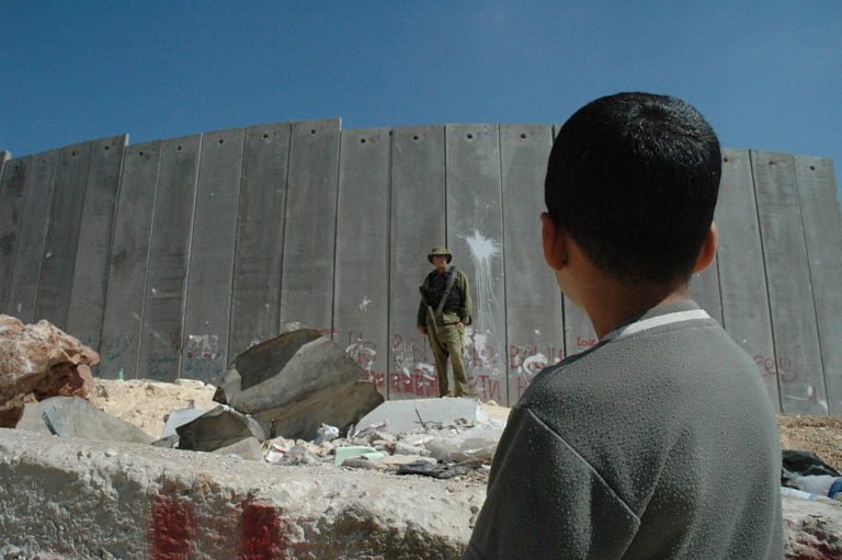 Un garçon palestinien et un soldat israélien devant la barrière israélienne de Cisjordanie.
