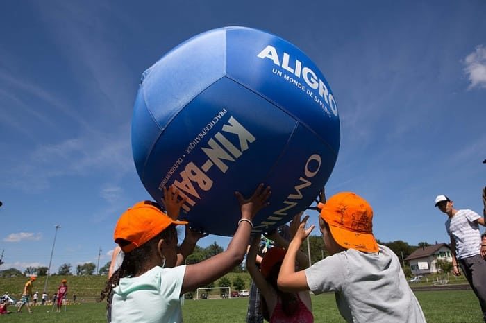 des enfants sont en train de soulever à trois un ballon géant au-dessus de leur tête