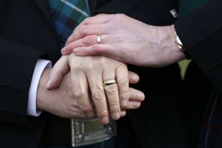 Les mains de deux personnes en soutane, portant une alliance, sont posées les unes au dessus des autres.