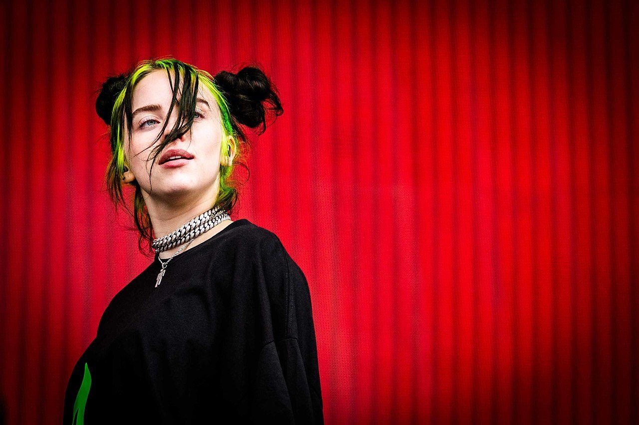 La chanteuse Billie Eilish, habillée de noir devant un fond rouge