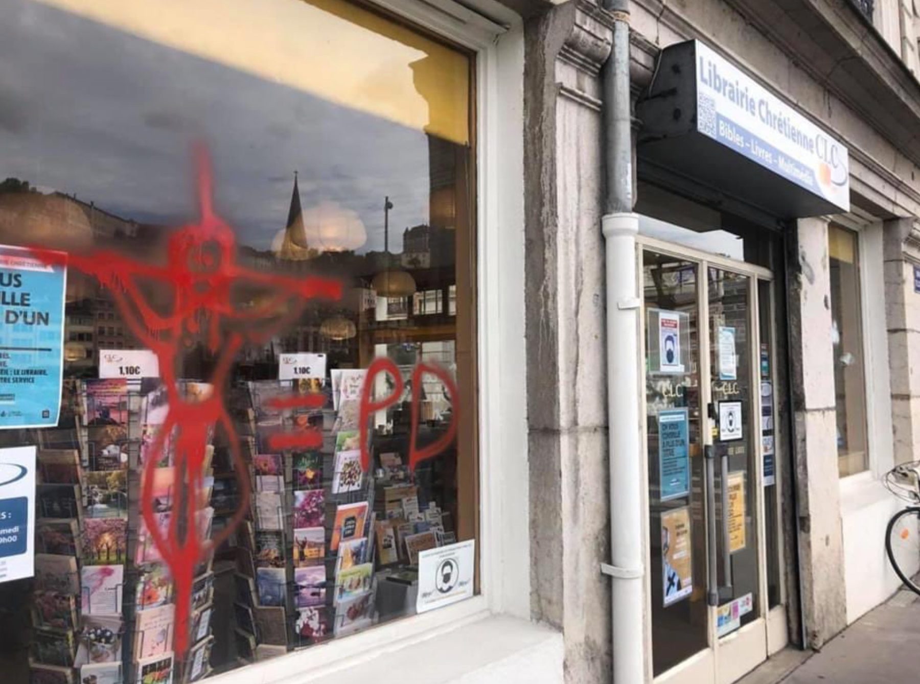 vitrine d'une librairie chrétienne taguée d un christ en croix suivi d une insulte