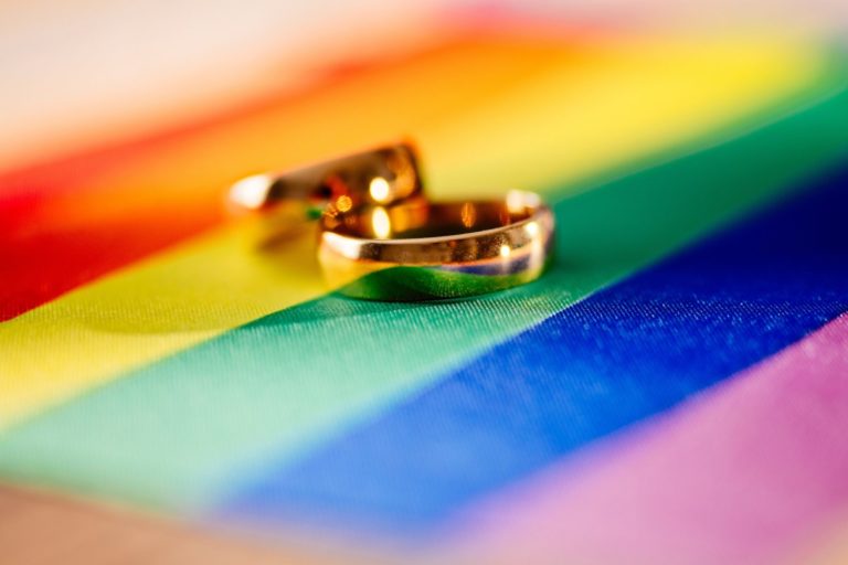 Photo symbole : deux alliances en or posées sur un drapeau arc-en-ciel