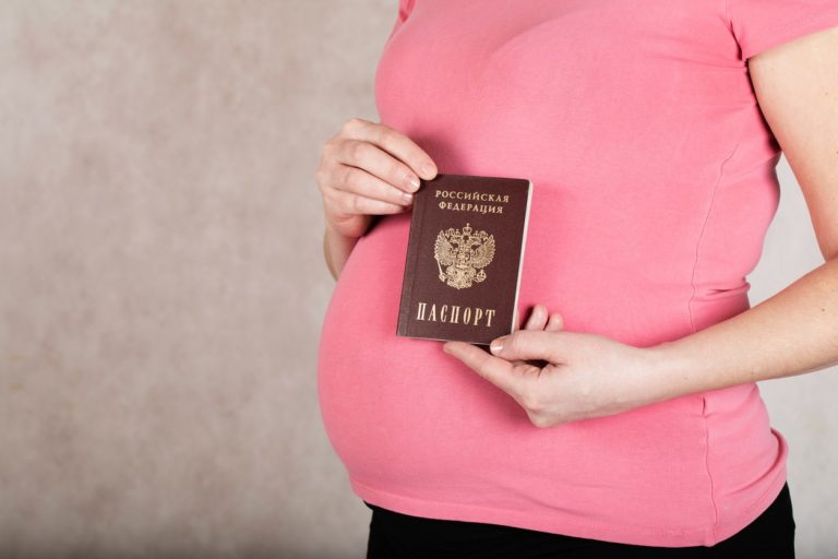 Une jeune femme enceinte tient son passeport russe devant son ventre