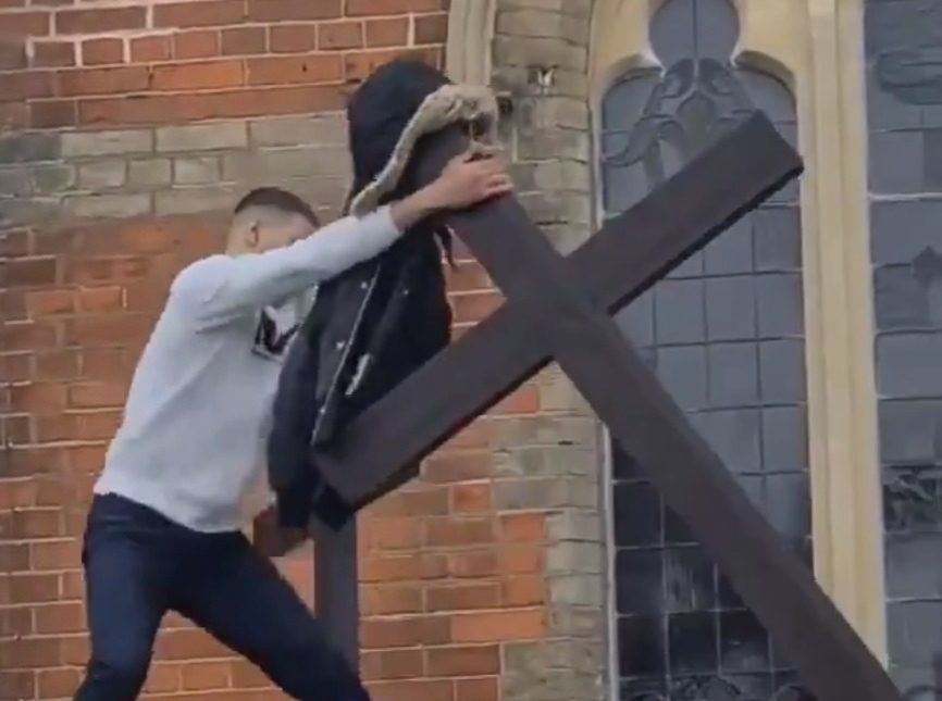 Un jeune homme en train d'arracher une croix en bois de son socle sur le toit d'une église de l'Est de Londres