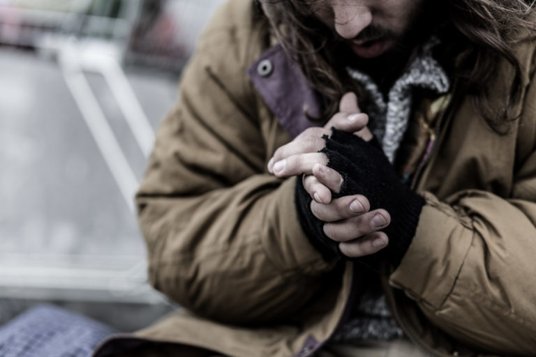 une personne sans abri à la rue les mains jointes a cause du froid et du manque
