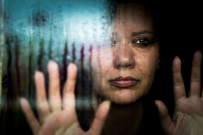 Une femme déprimée regardant la pluie tomber par la fenêtre pour illustrer la souffrance