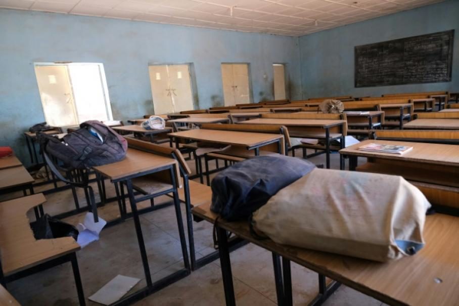 Dans une salle de classe vétuste, plusieurs sacs de voyage sont posés sur les pupitres.