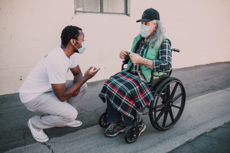 Un soignant se tient agenouillé devant une personne en fauteuil roulant