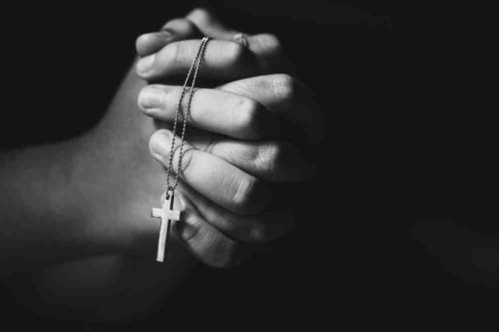 Mains en prière tenant une croix