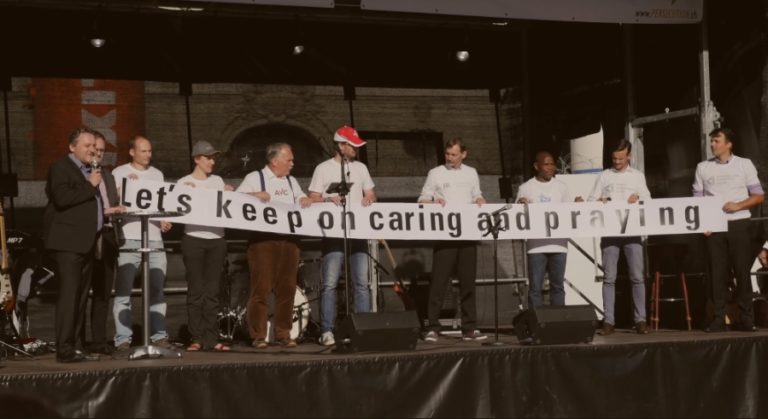 Sur scène, déploiement d'une banderole "Let's keep on caring and praying"