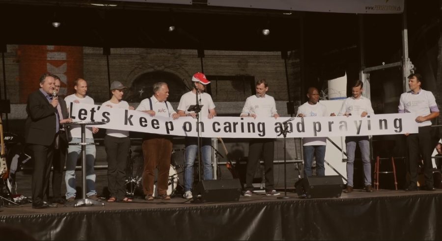 Sur scène, déploiement d'une banderole "Let's keep on caring and praying"