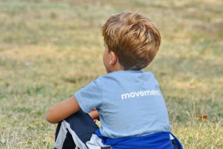 Un petit garçon blond est assis dans l'herbe, de dos