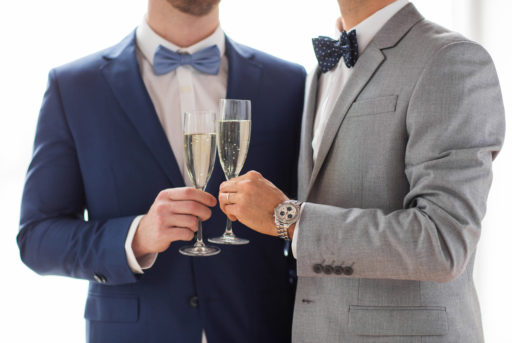 Un couple d'hommes en costume trinque avec des coupes de champagne.