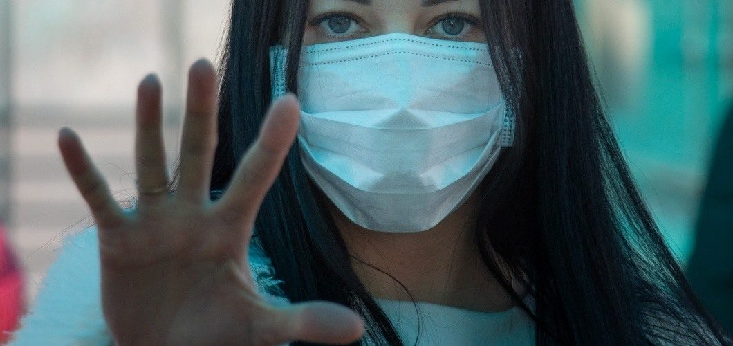 Une jeune femme portant un masque chirurgical fait signe de s'arrêter avec la main