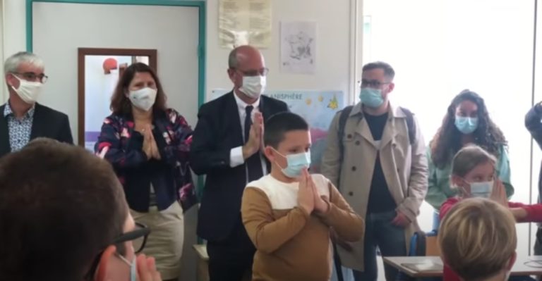 Jean-Michel Blanquer et des élèves dans une classe, mains jointes