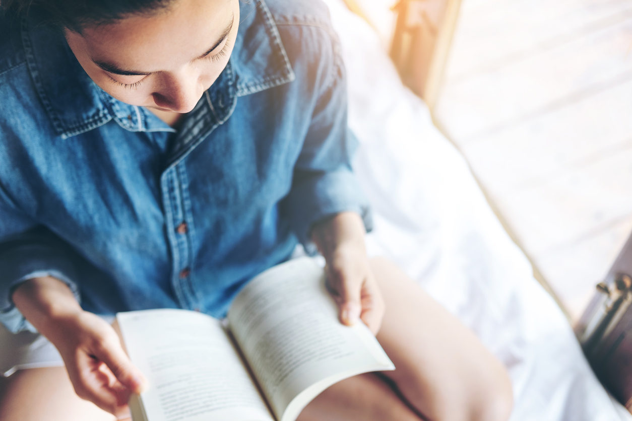 Une adolescente assise lit la Bible, qui est posé sur ses genoux. Vue plongeante