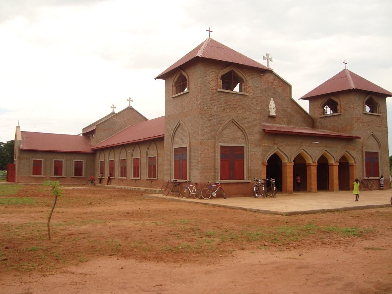 Vue d'une Eglise catholique soudanaise. Elle est grande, en pierre, avec des formes carrées et des toîts rouges surmontés de croix..