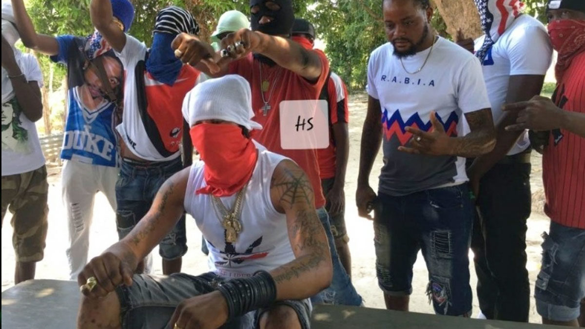Un membre du gang haïtien "400 mawozo" est assis, au premier plan, la tête et le bas du visage couverts par des foulards. Derrière lui, d'autres membres du gang, debout