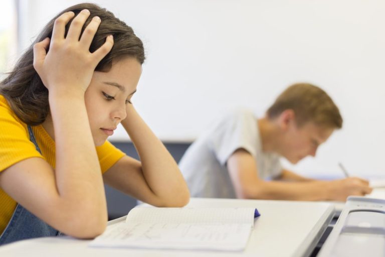 Une petite fille lit un manuel en classe, la tête posée sur ses deux mains