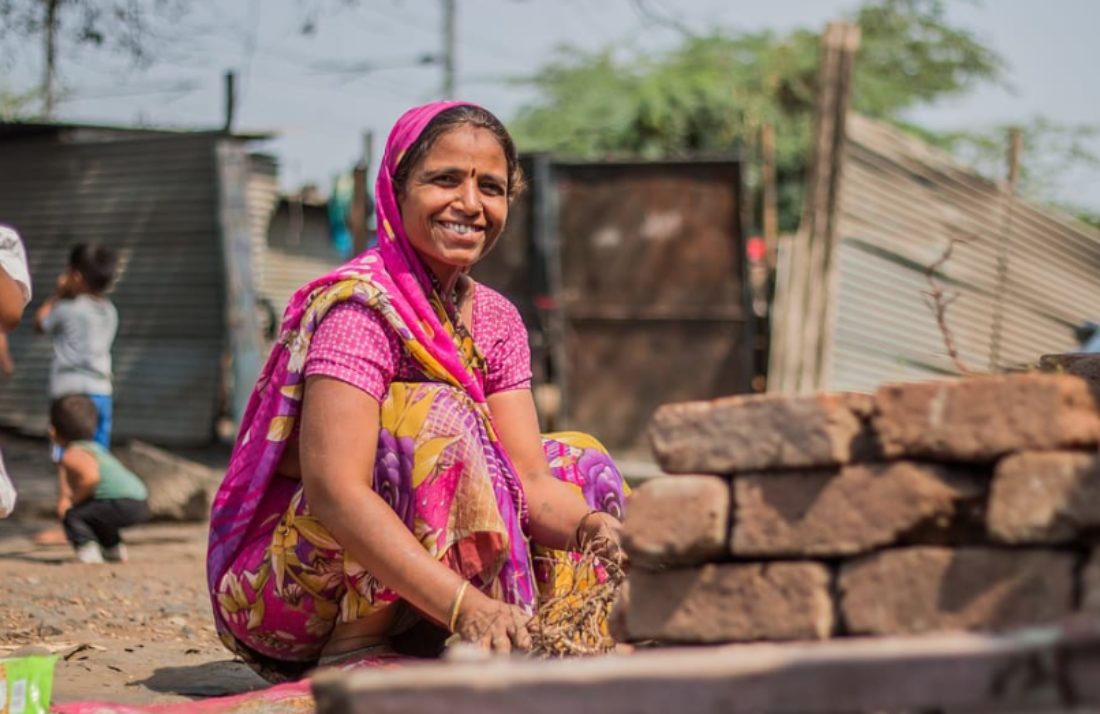 Une femme indienne vêtue de rose, assise au sol, sourit en direction de l'objectif
