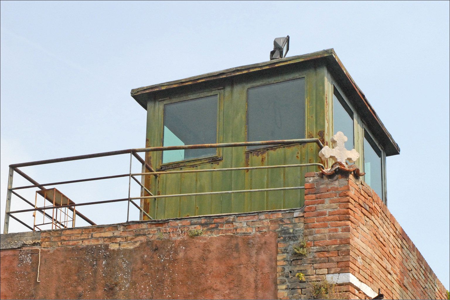 Vue en contre-plongée de la vigie d'un bâtiment en mauvais état, en briques et en tôle. Fond de ciel gris.