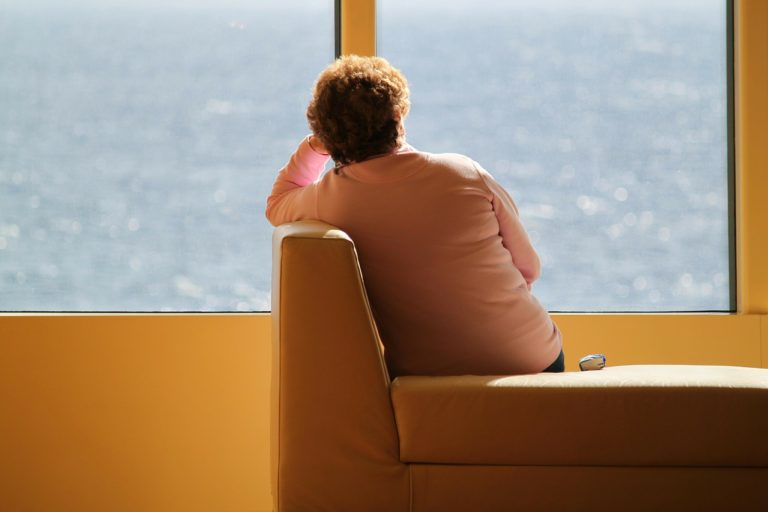 Une femme au cheveux court est assise, de dos à l'objectif, sur la banquette d'un commerce. Elle regarde vers une fenêtre opaque. Son coude est posé sur le dossier .et elle semble réfléchir.