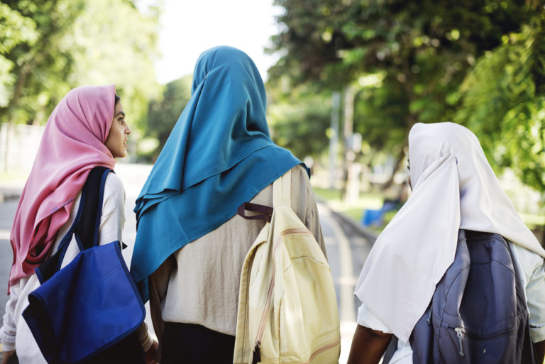 Groupe de femmes moyen-orientales de dos. Elles marchent en discutant sur une route bordée d'arbres