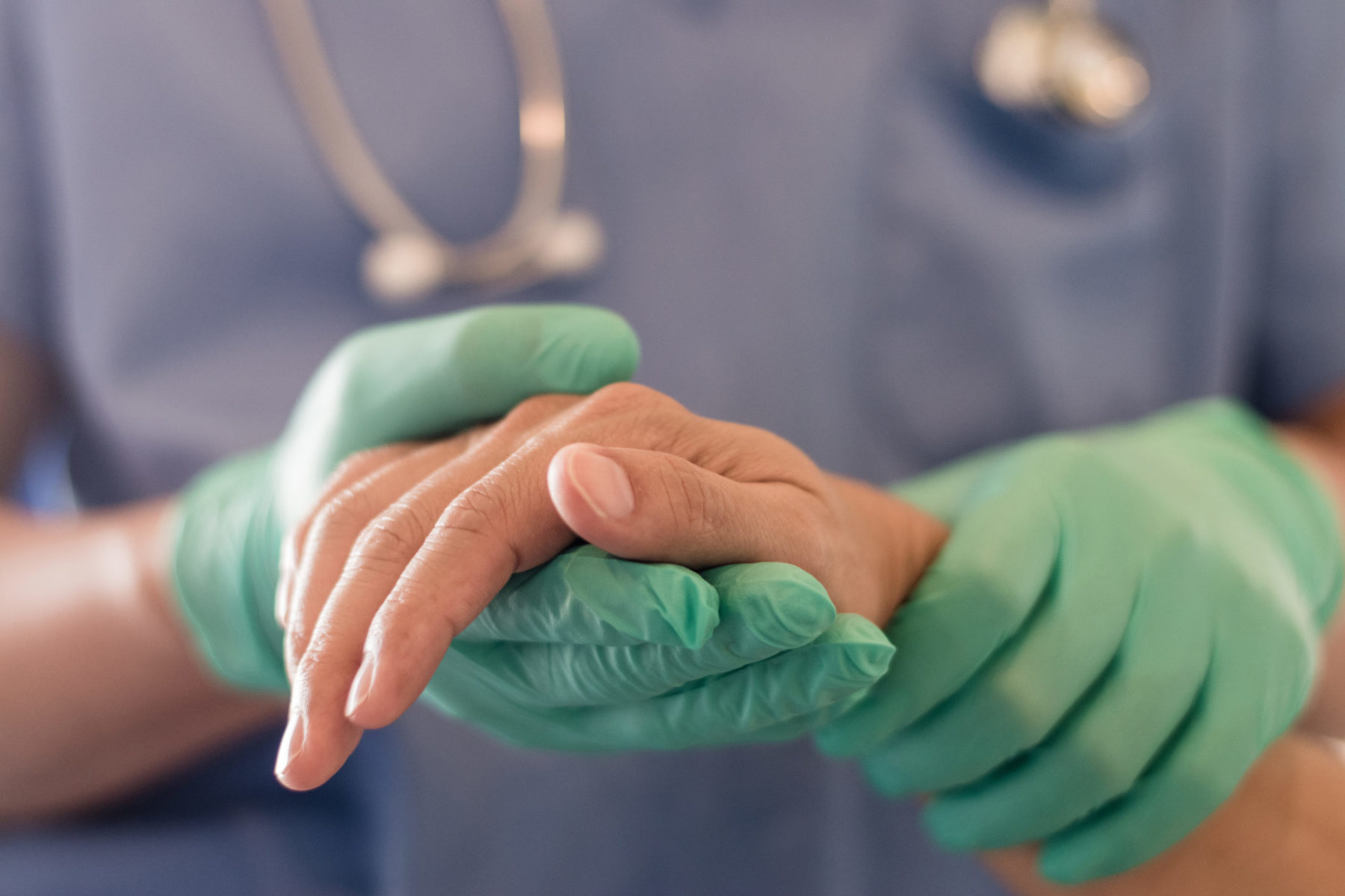 Les mains d'un soignant, gantés de latex vert, tiennent la main d'un patient
