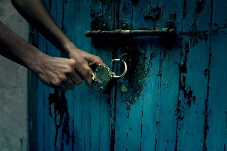 Des mains ouvrent un cadenas fixé à une porte bleue