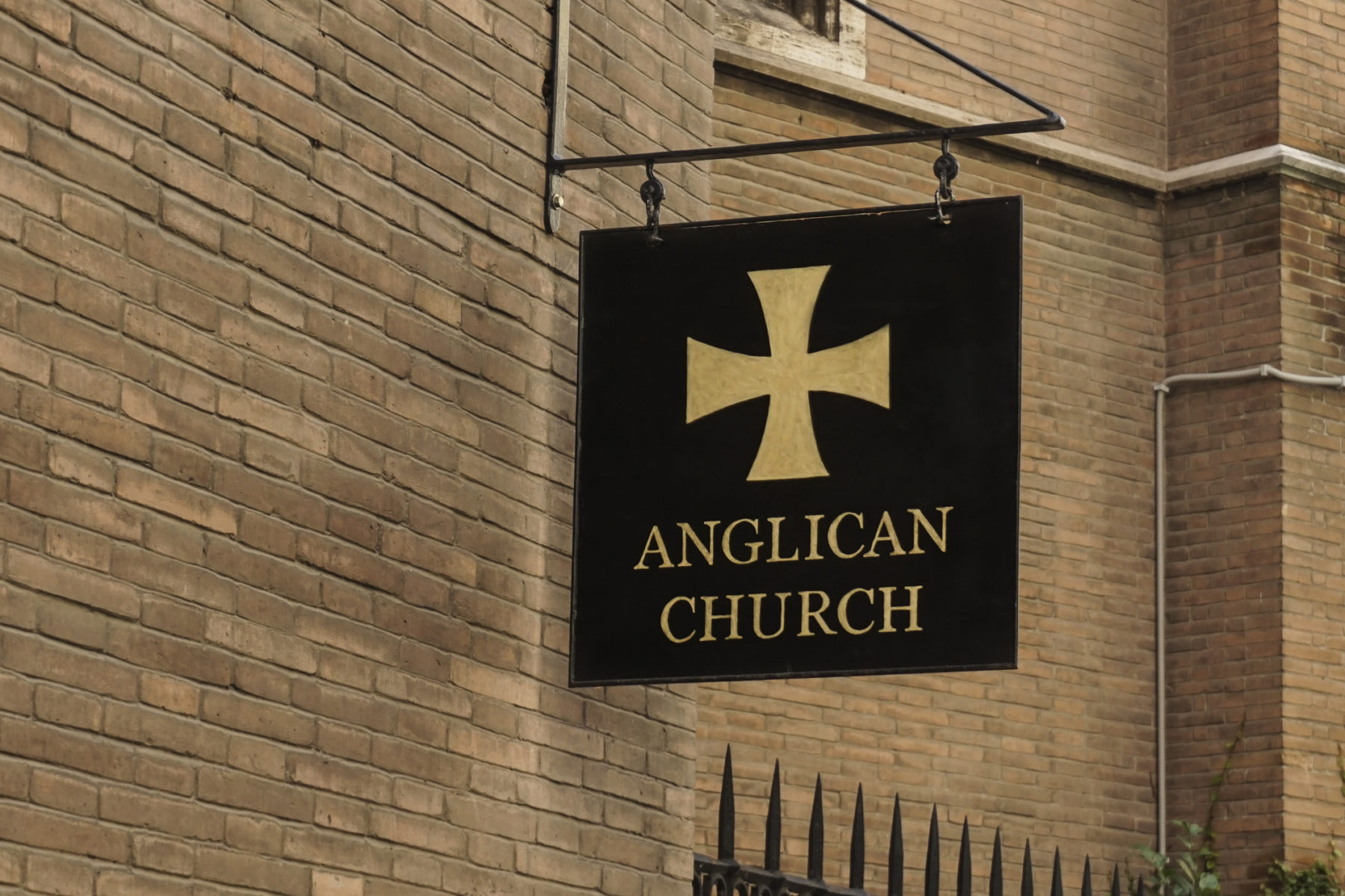 Enseigne d'une Eglise anglican fixée à un mur. Sur fond noir, une croix dorée, ainsi que les mots "Anglican Church" apparaissent.