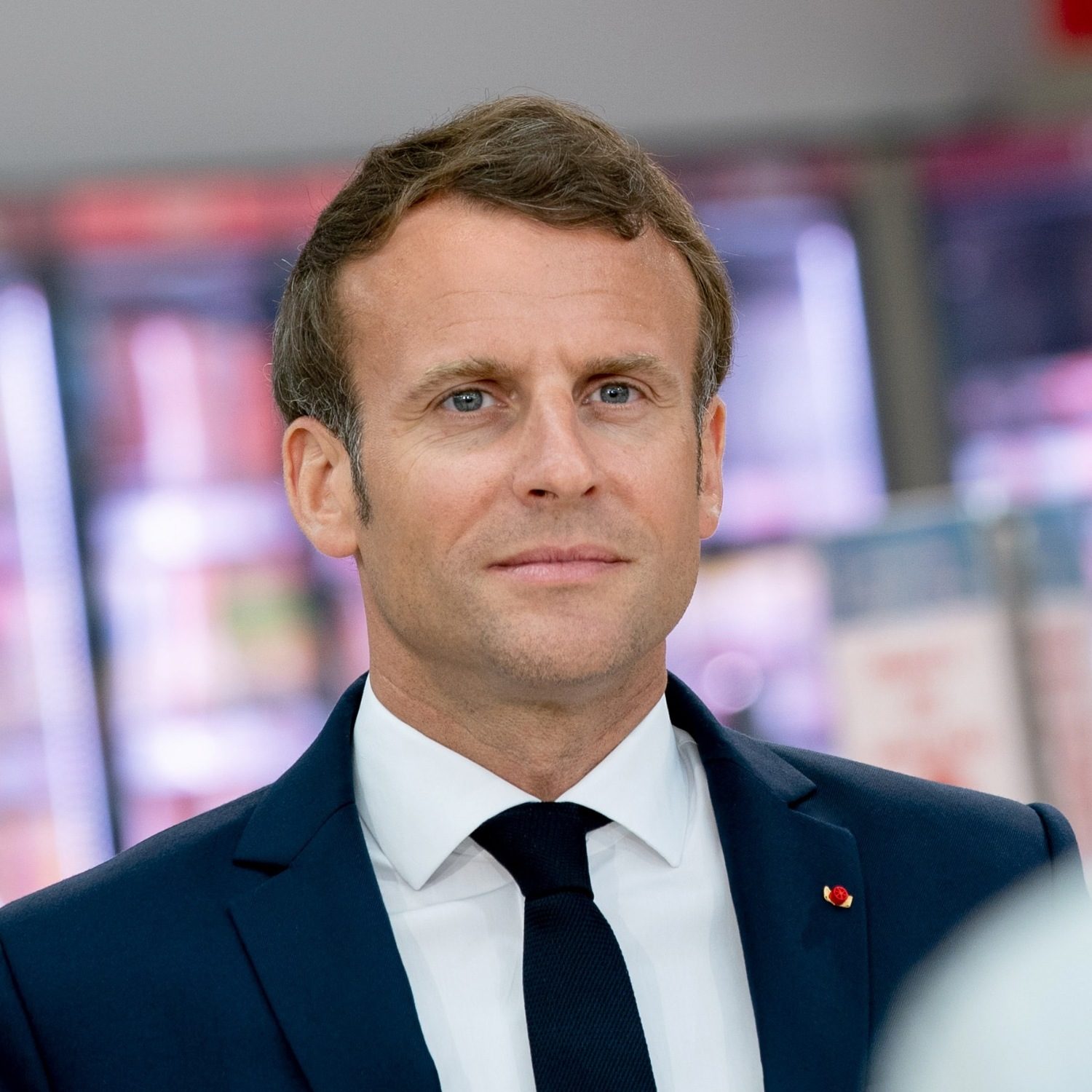 Photo coupée aux épaules d'Emmanuel macron, cheveux brun clair en costume-cravate sombre. Pas tout à fait face à l'objectif, il regarde au loin