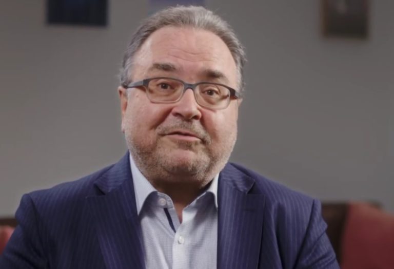 Photo portrait de l'évêque Michael Chalupka. Il porte des lunettes, un costume bleu foncé et des cheveux gris. Face à l'objectif, il est en train de parler