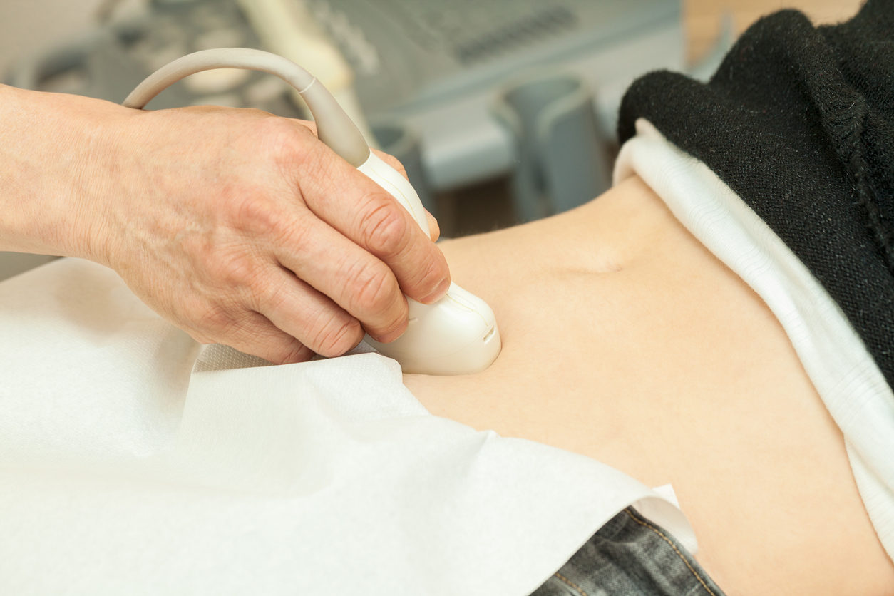 Un soignant procède à une échographie. On ne voit que la main du médecin passant la sonde sur le ventre d'une femme.