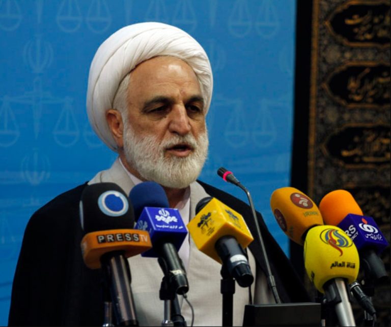 Gholam Hossein Mohseni Ejei, portant un turban blanc et une barbe blanche, parle devant plusieurs micros de différentes agences de presse
