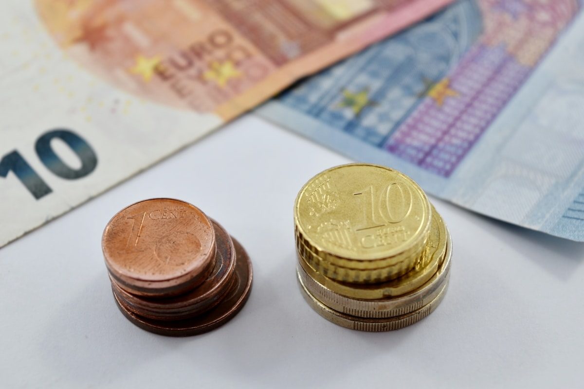 Deux petites piles de cents et deux petites piles de pièces d'euro jaunes sont posées à côté de deux billets de banques, de dix et vingt euros.