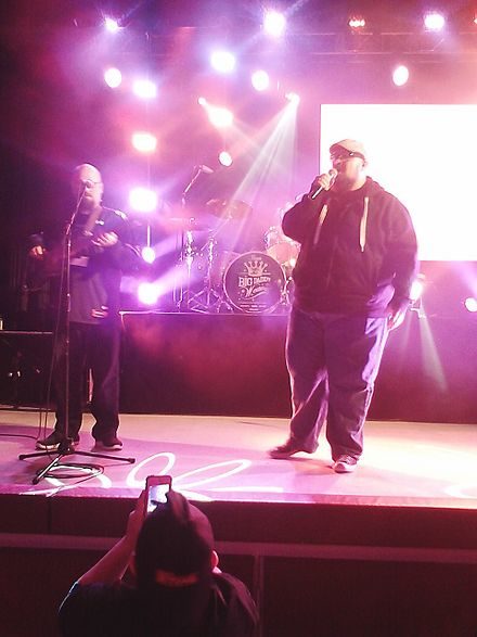 Concert du groupe Big Daddy Weave, dans une luminosité éblouissante violette. On voit sur la scène un chanteur avec un micro, et un guitariste. au premier plan, un spectateur filme la scène avec un smartphone.