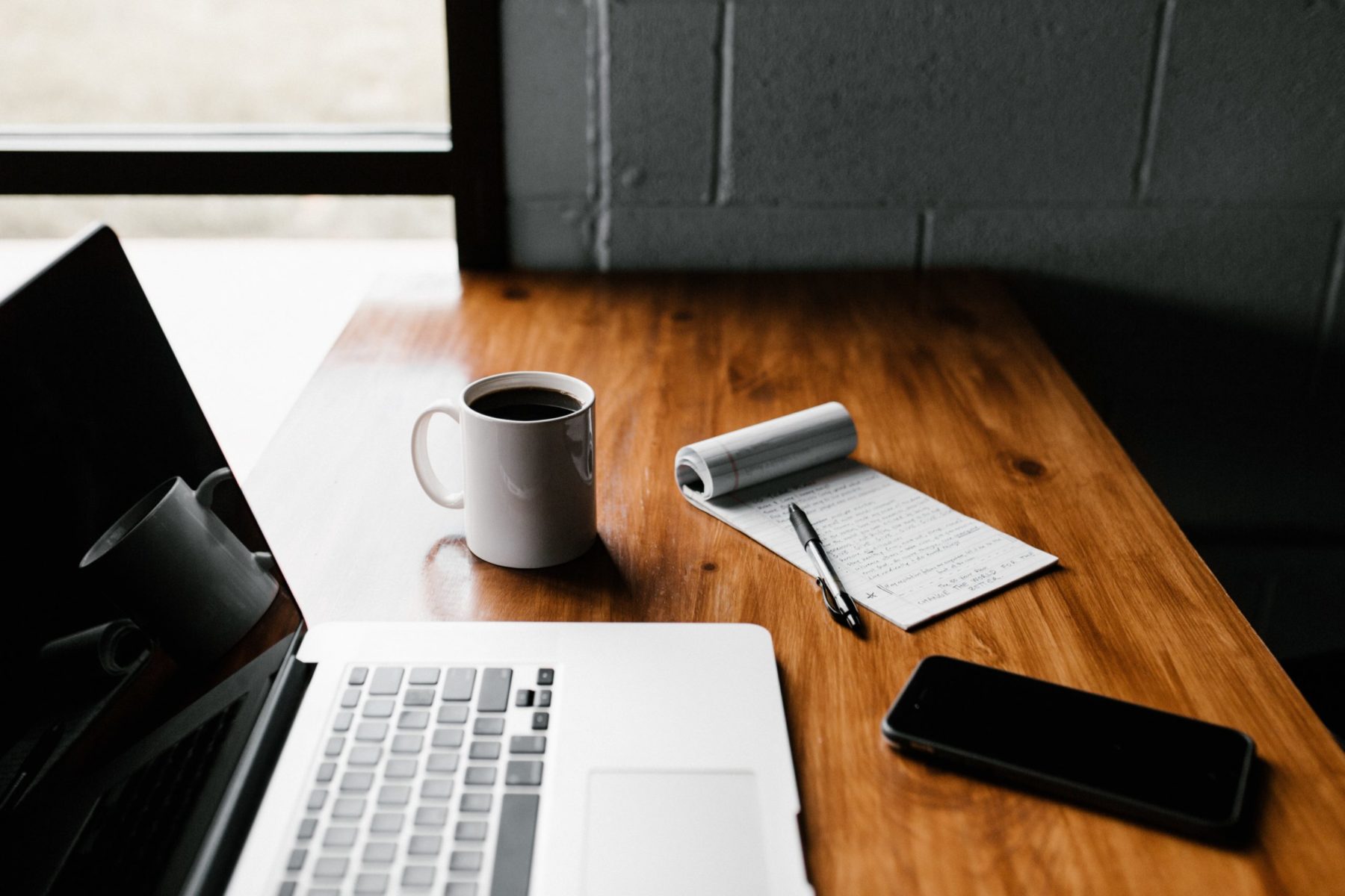 Sur un burau sont posés un ordinateur, une tasse de café, un bloc-notes et un smartphone