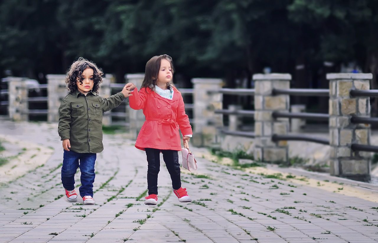 Deux petits enfants, un garçon et une fille, marchent en se tenant la main.