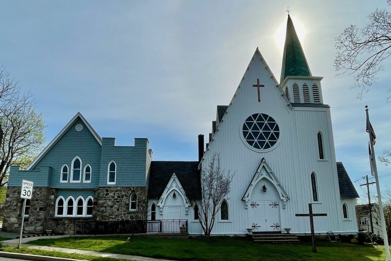 Vue de face d'une Eglise réformée, avec sa chapelle. Le bâtiment est blanc, pas très grand, avec une rosace et une croix fixée sur la façade. Le toit est en pointe, et possède un clocher. A gauche, la chapelle est une maison bleu avec des fenêtres en ogives.
