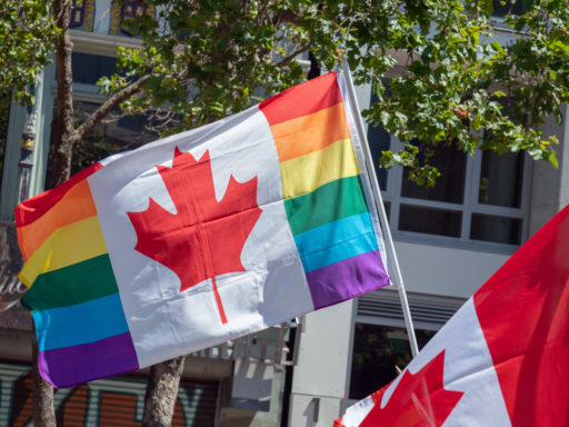 Un drapeau, mêlant les couleurs LGBT et celles du drapeau canadien, flotte au vent dans une rue.