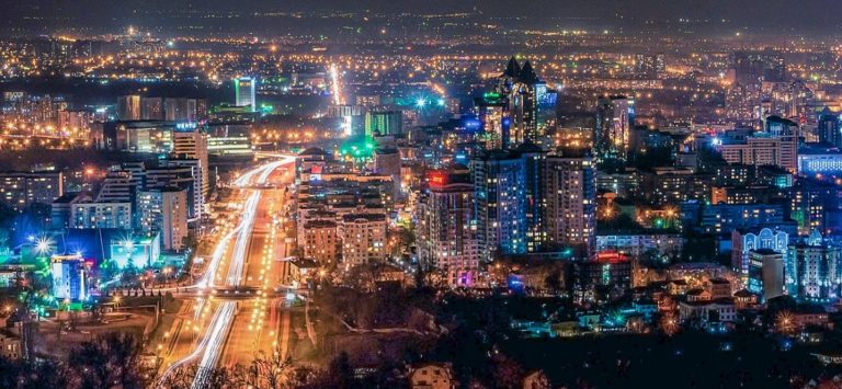 Vue aérienne, de nuit, de la ville d'Almaty. Les bâtiments sont illuminés et une grande route très éclairée se dessine à gauche