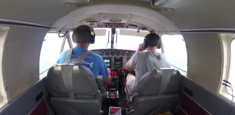 On voit deux hommes au commandes d'un petit avion de dos.