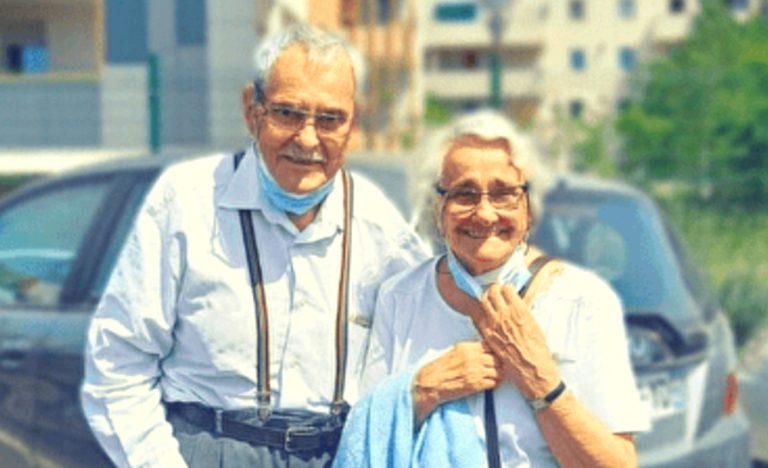 Jack Mouyon et son épouse Andrée, à l'âge de la retraite. Ils sourient tous deux vers l'objectif, masques anti-covid sous le menton. Derrière eux, une voiture, et plus loin, des HLM.