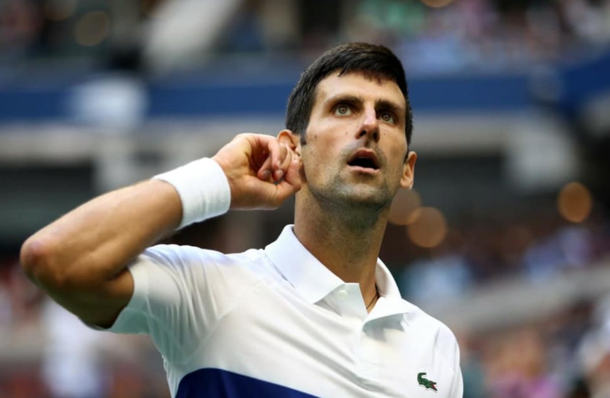 Novak Djokovic, jeune homme mince et brin, regarde vers le haut. Il touche son oreille de la main gauche, et semble inquiet.