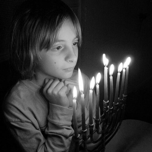 Photo en noir et blanc. Un enfant regarde de tout près les bougies d'un candélabre à neuf branches.