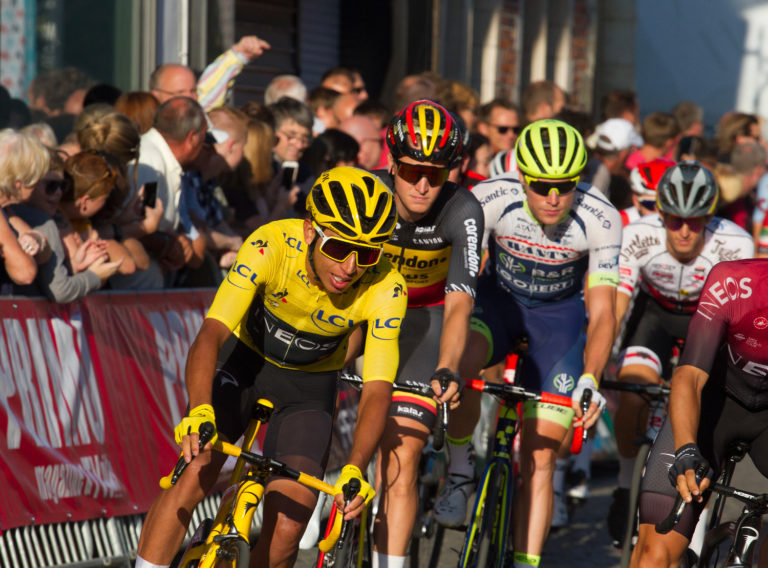 Le jeune colombien Egan Bernal, maillot et casque jaune, est en tête d'un peloton de cyclistes. La photo est prise presque de face. On voit la foule en arrière-plan.