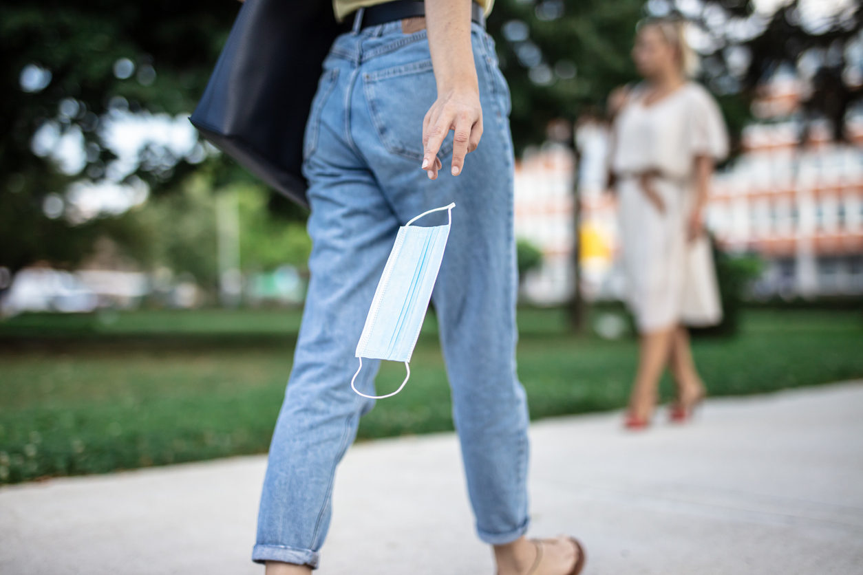 Une femme en jean marche en tenant son masque anti-covid à la main
