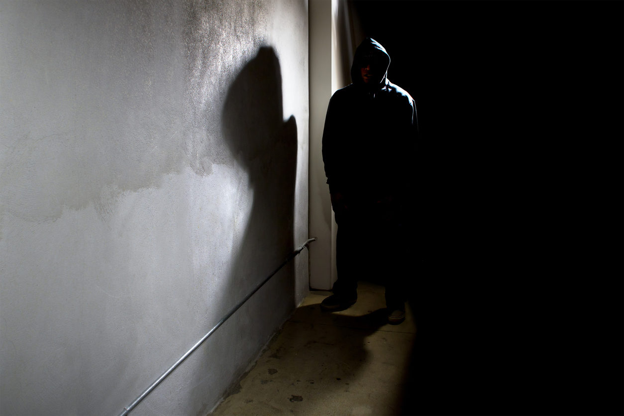 Un homme encapuchonné attend dans la pénombre, dans un couloir.