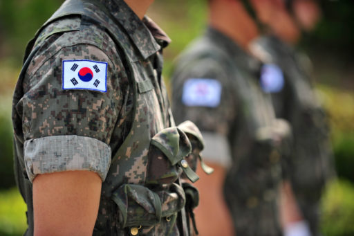Photo du buste d'un militaire coréen vue de profil. Il porte une réplique du drapeau sud-coréen sur l'épaule.